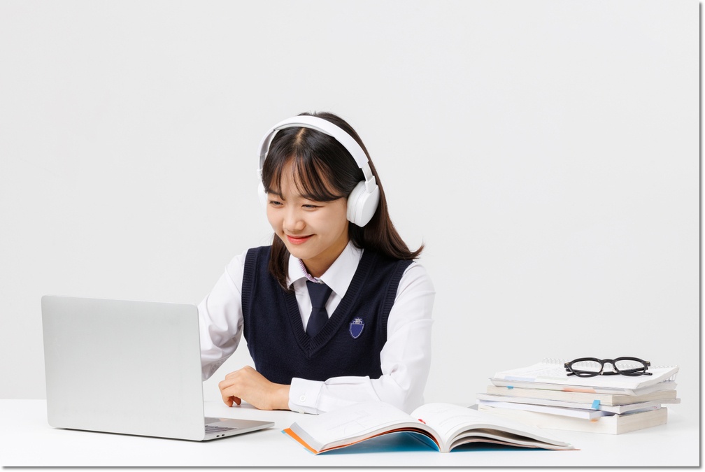 헤드폰을 쓰고 책과 노트북을 보는 학생